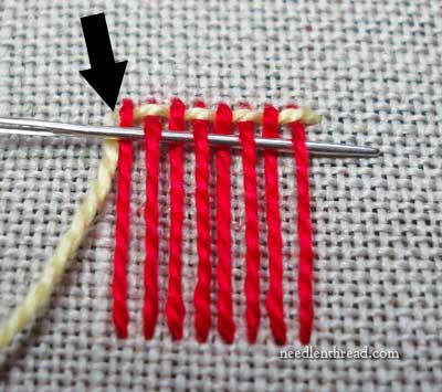 Showing a mending technique of weaving repair stitch process with red thread vertical and beige thread horizontal on blue fabric. 